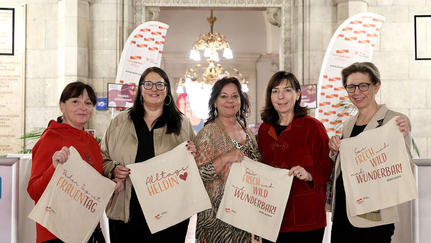 Die fünf Frauen stehen im Wiener Rathaus und halten jeweils eine Stofftasche mit Sprüchen zum Frauentag in Händen.