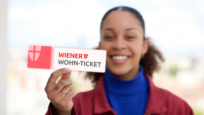 Frau hält ein Ticket mit der Aufschrift 'WIENER WOHN-TICKET' in die Kamera und lächelt
