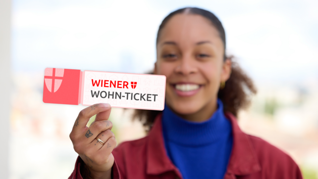 Frau hält ein Ticket mit der Aufschrift 'WIENER WOHN-TICKET' in die Kamera und lächelt