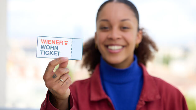 Imagebild, eine junge Frau hält ein Wiener Wohn-Ticket direkt in die Kamera, sie ist unscharf im Hintergrund, das Wohn-Ticket im Vordergrund